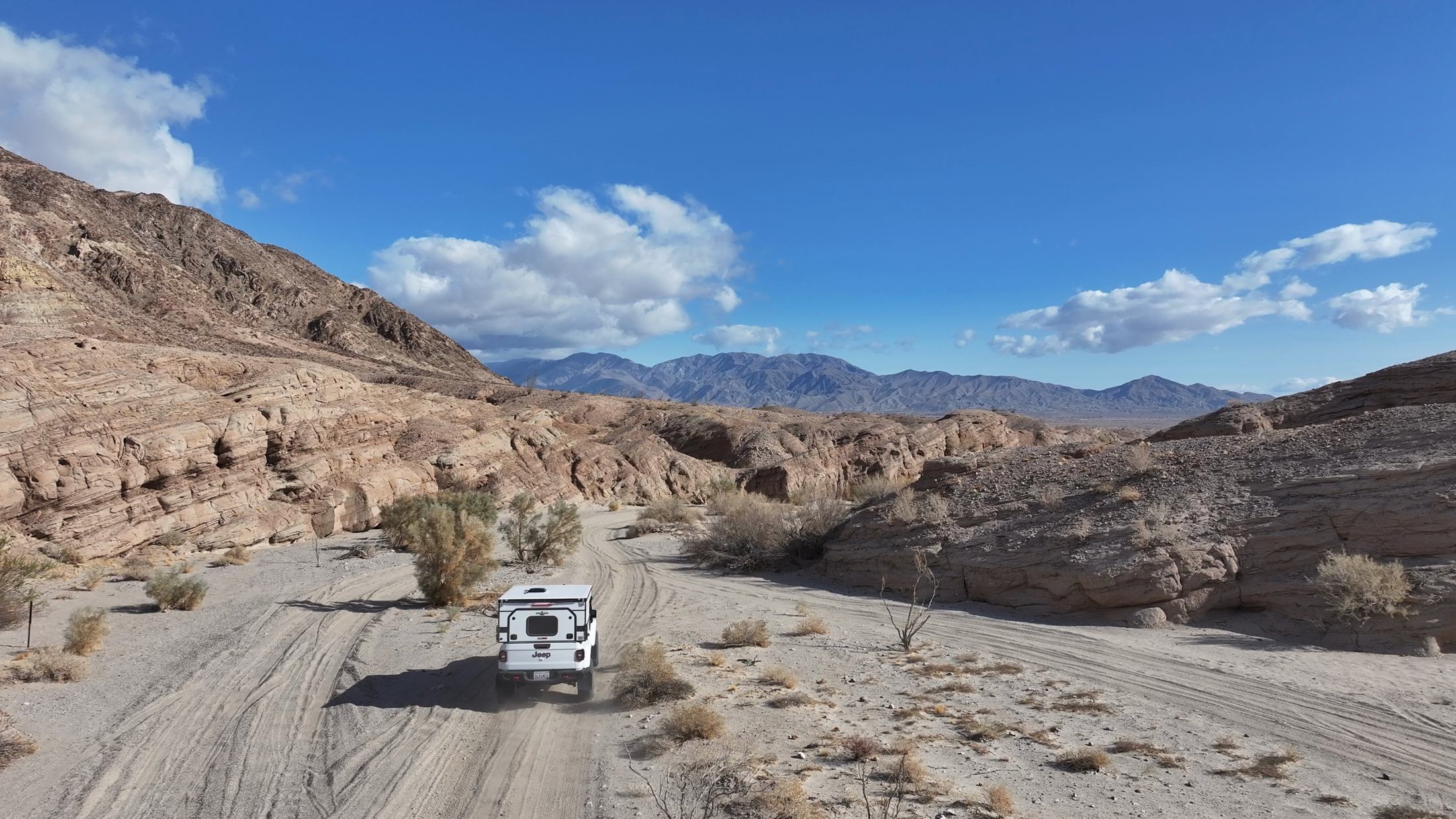 A white Jeep driving up a sandy wash between eroded canyon walls in Anza-Borrego Desert State Park