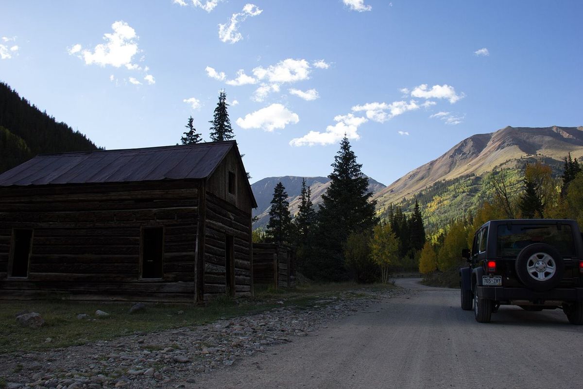 A Jeep on a dirt road past an old log cabin in the San Juan Mountains